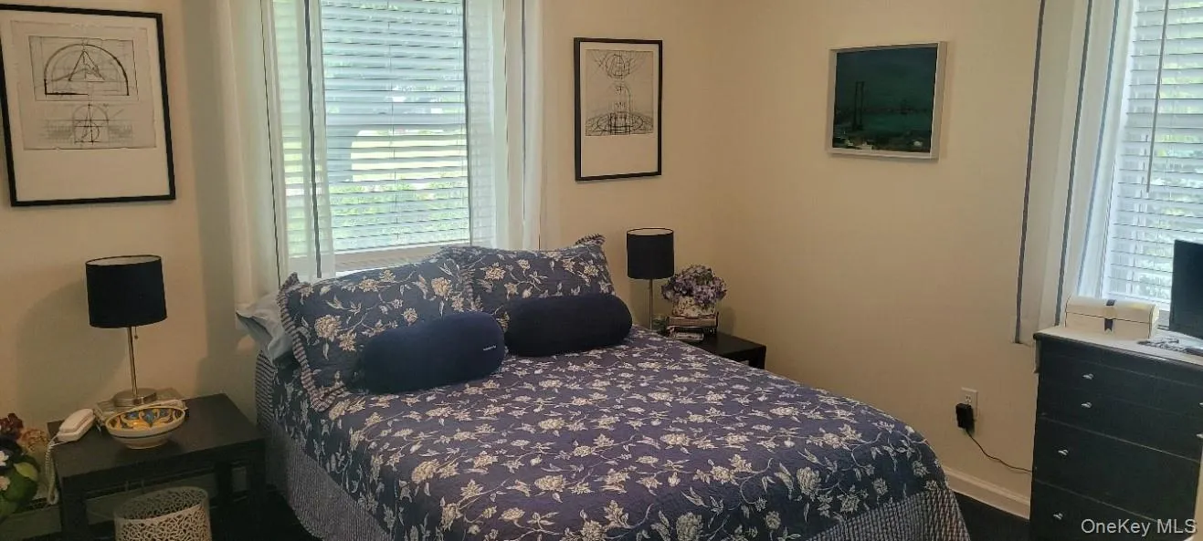 Second Bedroom featuring two windows with horizontal blinds and sheer curtains, a built-in baseboard, and wood-finish flooring Second Bedroom featuring two windows with horizontal blinds and sheer curtains, a built-in baseboard, and wood-finish flooring