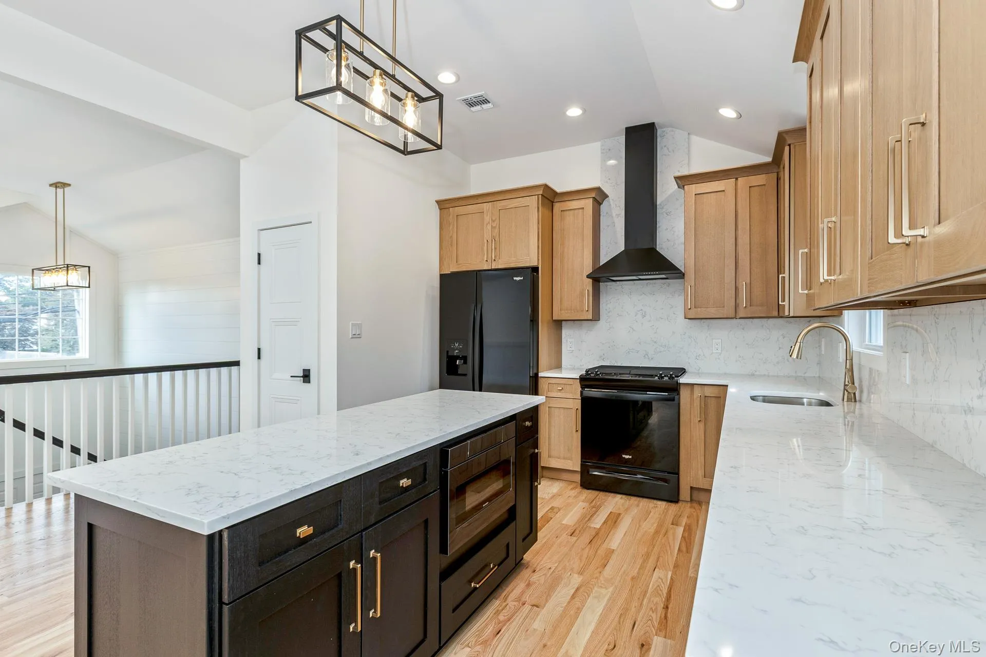 Kitchen featuring light stone counters, decorative light fixtures, vaulted ceiling, black appliances, and wall chimney range hood Kitchen featuring light stone counters, decorative light fixtures, vaulted ceiling, black appliances, and wall chimney range hood