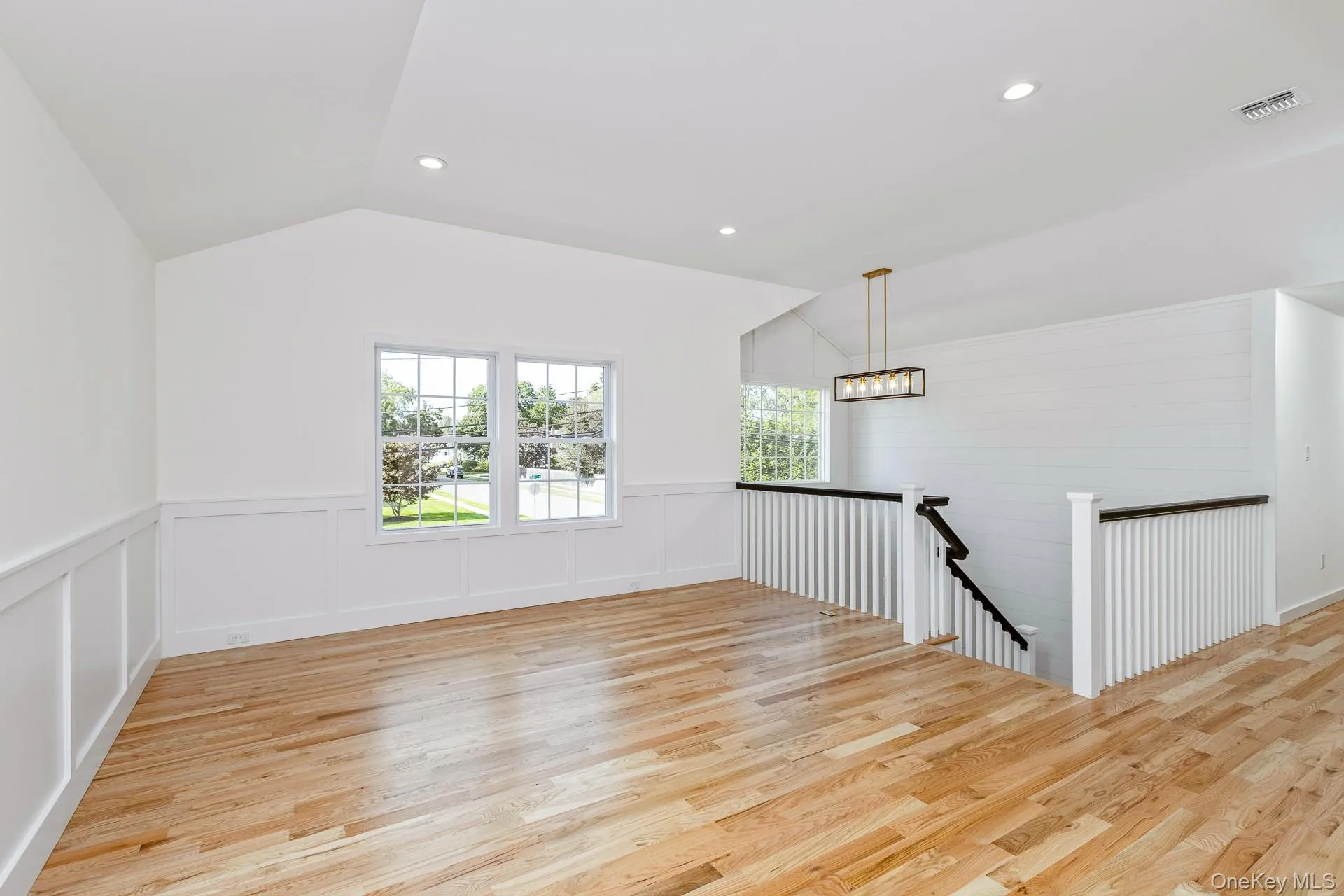 Unfurnished room with light wood finished floors, recessed lighting, lofted ceiling, a decorative wall, and wainscoting Unfurnished room with light wood finished floors, recessed lighting, lofted ceiling, a decorative wall, and wainscoting