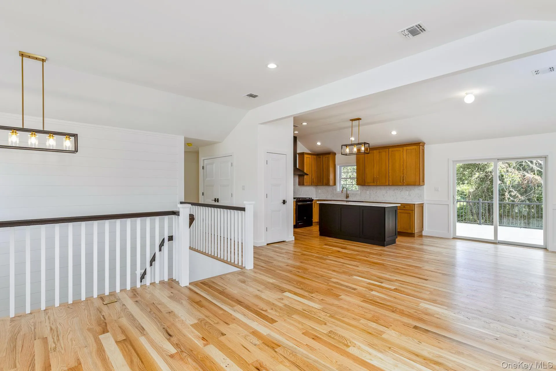Kitchen with hanging light fixtures, brown cabinetry, lofted ceiling, light wood finished floors, and open floor plan Kitchen with hanging light fixtures, brown cabinetry, lofted ceiling, light wood finished floors, and open floor plan