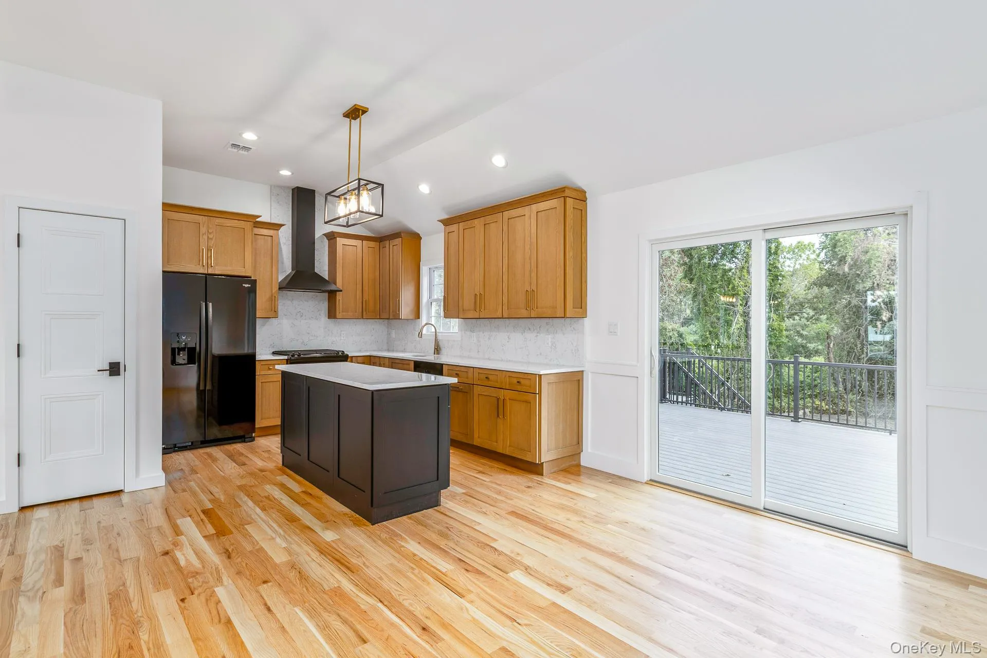 Kitchen featuring hanging light fixtures, decorative backsplash, black fridge, a center island, and light wood-type flooring Kitchen featuring hanging light fixtures, decorative backsplash, black fridge, a center island, and light wood-type flooring