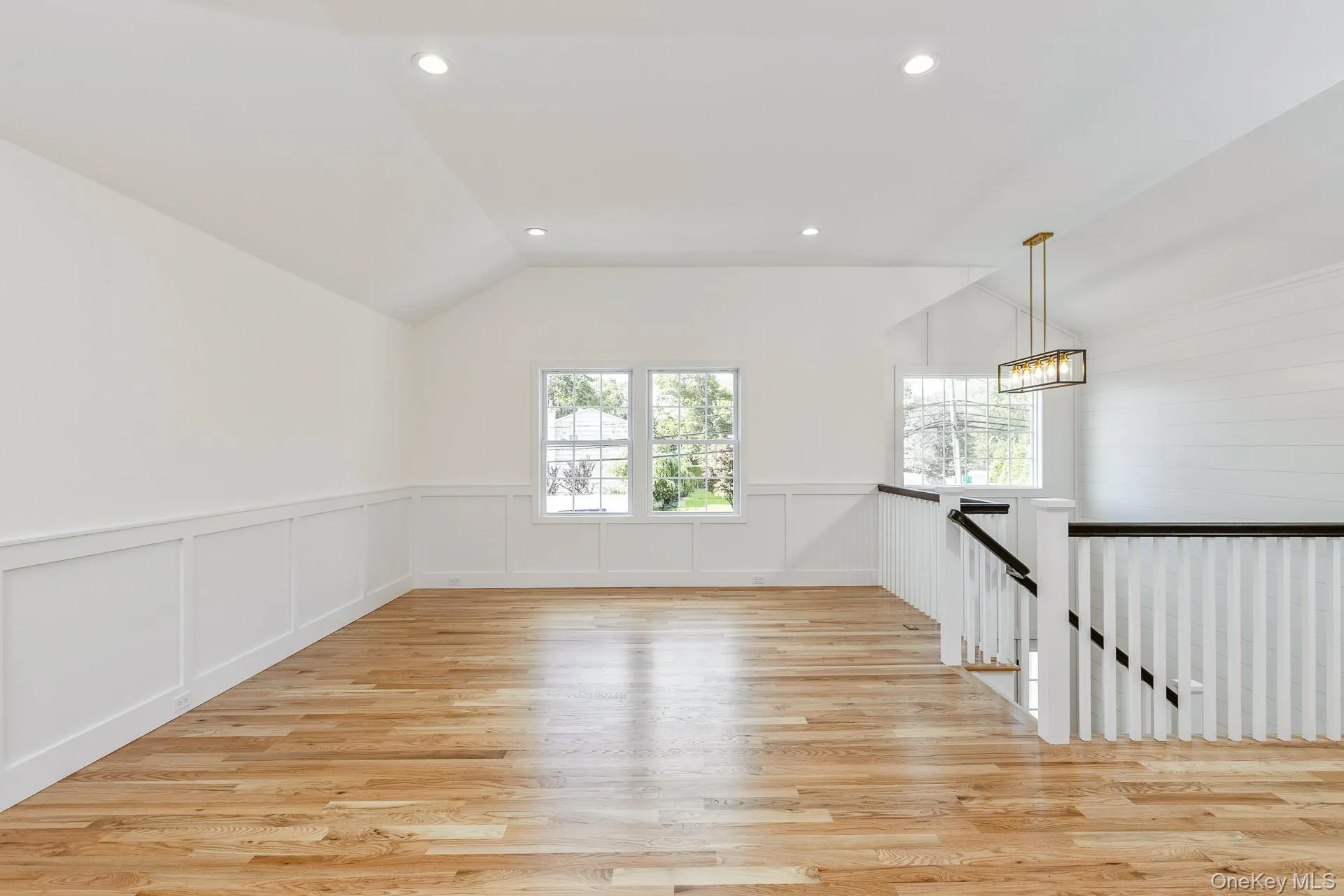 Empty room featuring lofted ceiling, light wood-type flooring, recessed lighting, a decorative wall, and wainscoting Empty room featuring lofted ceiling, light wood-type flooring, recessed lighting, a decorative wall, and wainscoting