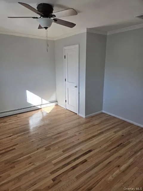 Hardwood flooring with a natural finish, crown molding, a white interior door with dark hardware, a ceiling fan with light fixture, and light gray wall paint Hardwood flooring with a natural finish, crown molding, a white interior door with dark hardware, a ceiling fan with light fixture, and light gray wall paint