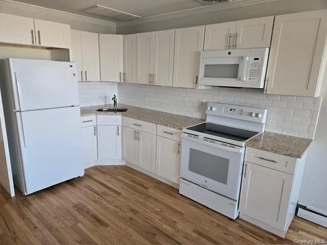 Kitchen featuring white shaker cabinetry, light-toned granite-style countertops, subway tile backsplash, stainless steel sink with a gooseneck faucet, and wood-finish flooring Kitchen featuring white shaker cabinetry, light-toned granite-style countertops, subway tile backsplash, stainless steel sink with a gooseneck faucet, and wood-finish flooring