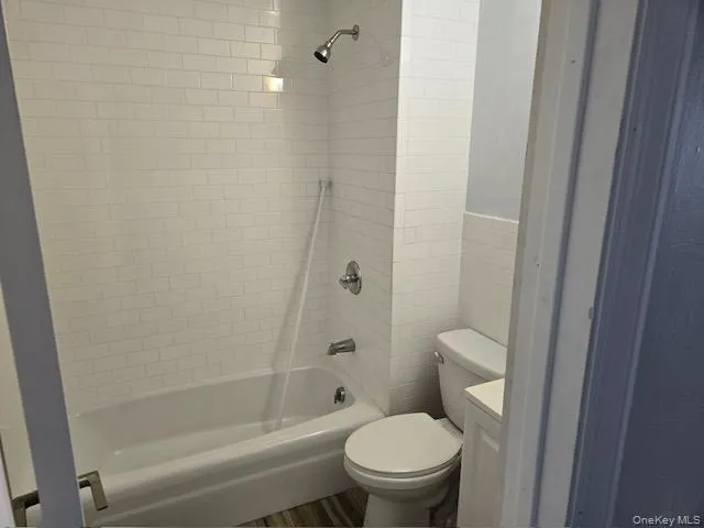 Bathroom featuring a white subway tile surround, white bathtub, chrome showerhead, and a toilet with a white tank Bathroom featuring a white subway tile surround, white bathtub, chrome showerhead, and a toilet with a white tank