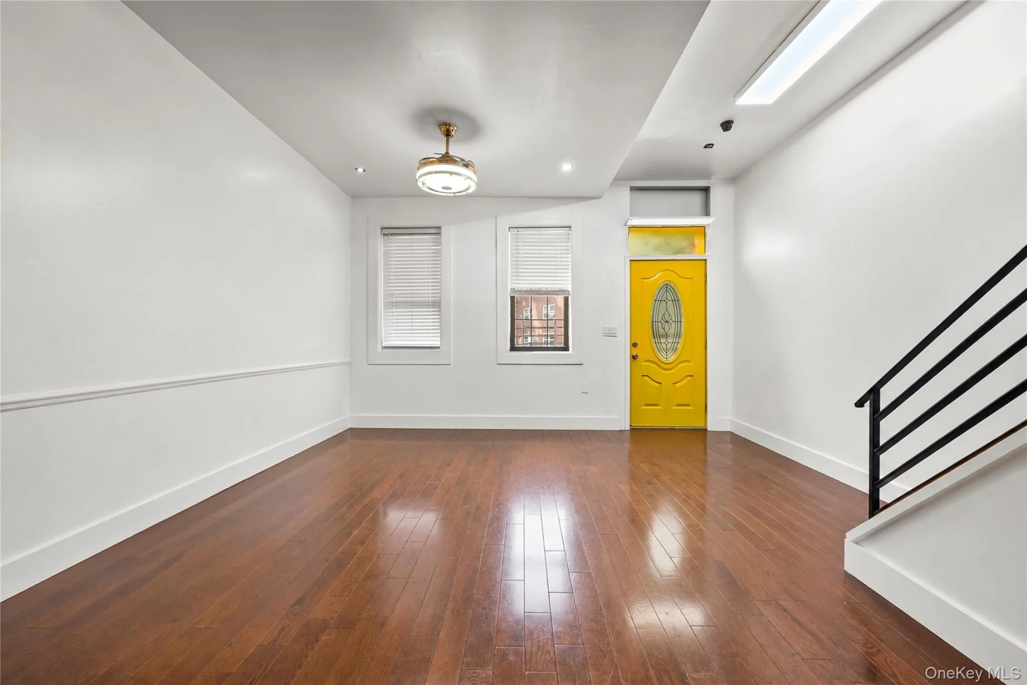 Open concept living space featuring wood-finish flooring and a bright yellow entry door with oval glass insert Open concept living space featuring wood-finish flooring and a bright yellow entry door with oval glass insert
