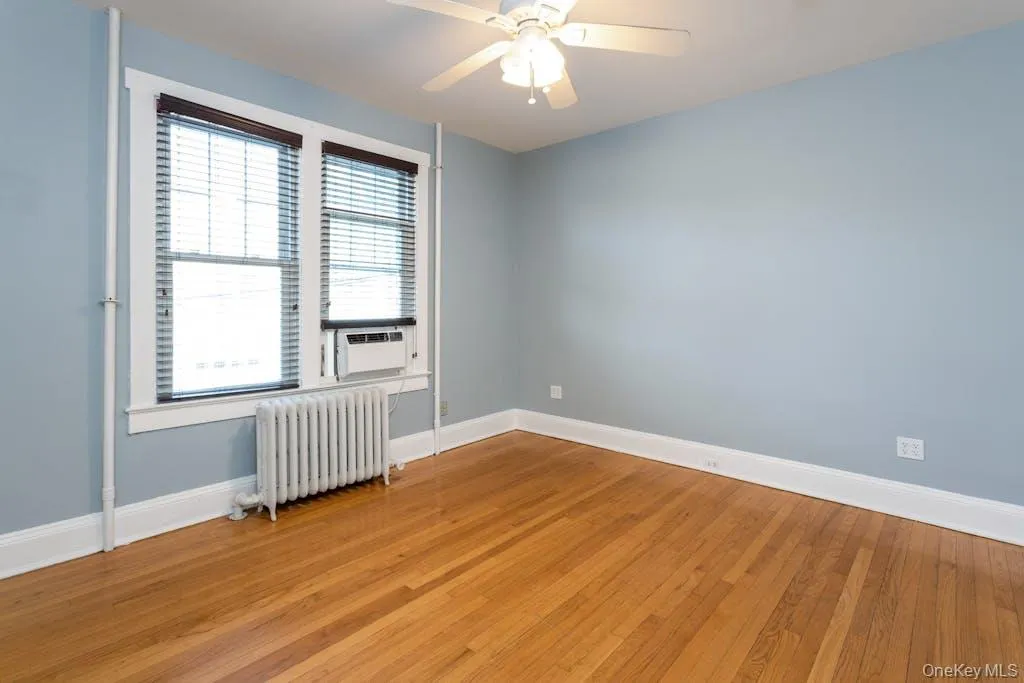 Unfurnished room with radiator heating unit, light hardwood / wood-style floors, cooling unit, and ceiling fan Unfurnished room with radiator heating unit, light hardwood / wood-style floors, cooling unit, and ceiling fan