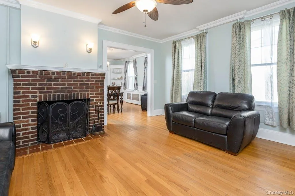 Living room featuring ceiling fan, wood-type flooring, ornamental molding, and a healthy amount of sunlight Living room featuring ceiling fan, wood-type flooring, ornamental molding, and a healthy amount of sunlight