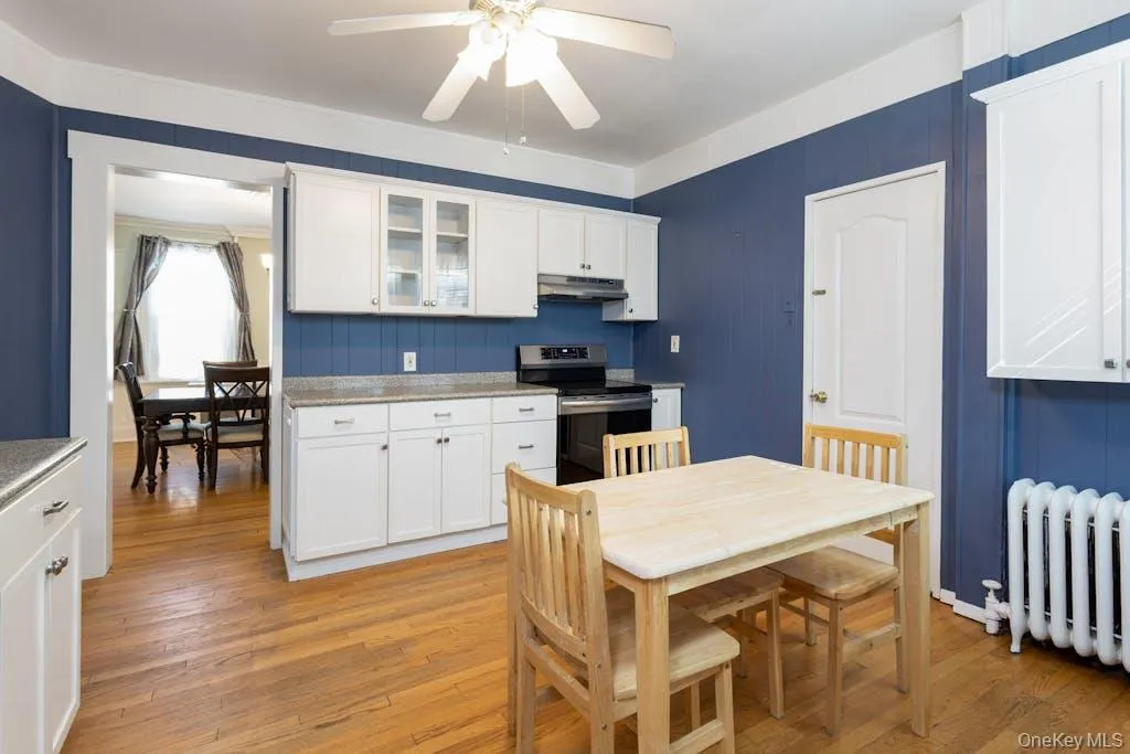 Kitchen with ceiling fan, radiator heating unit, white cabinetry, light wood-type flooring, and stainless steel electric range oven Kitchen with ceiling fan, radiator heating unit, white cabinetry, light wood-type flooring, and stainless steel electric range oven