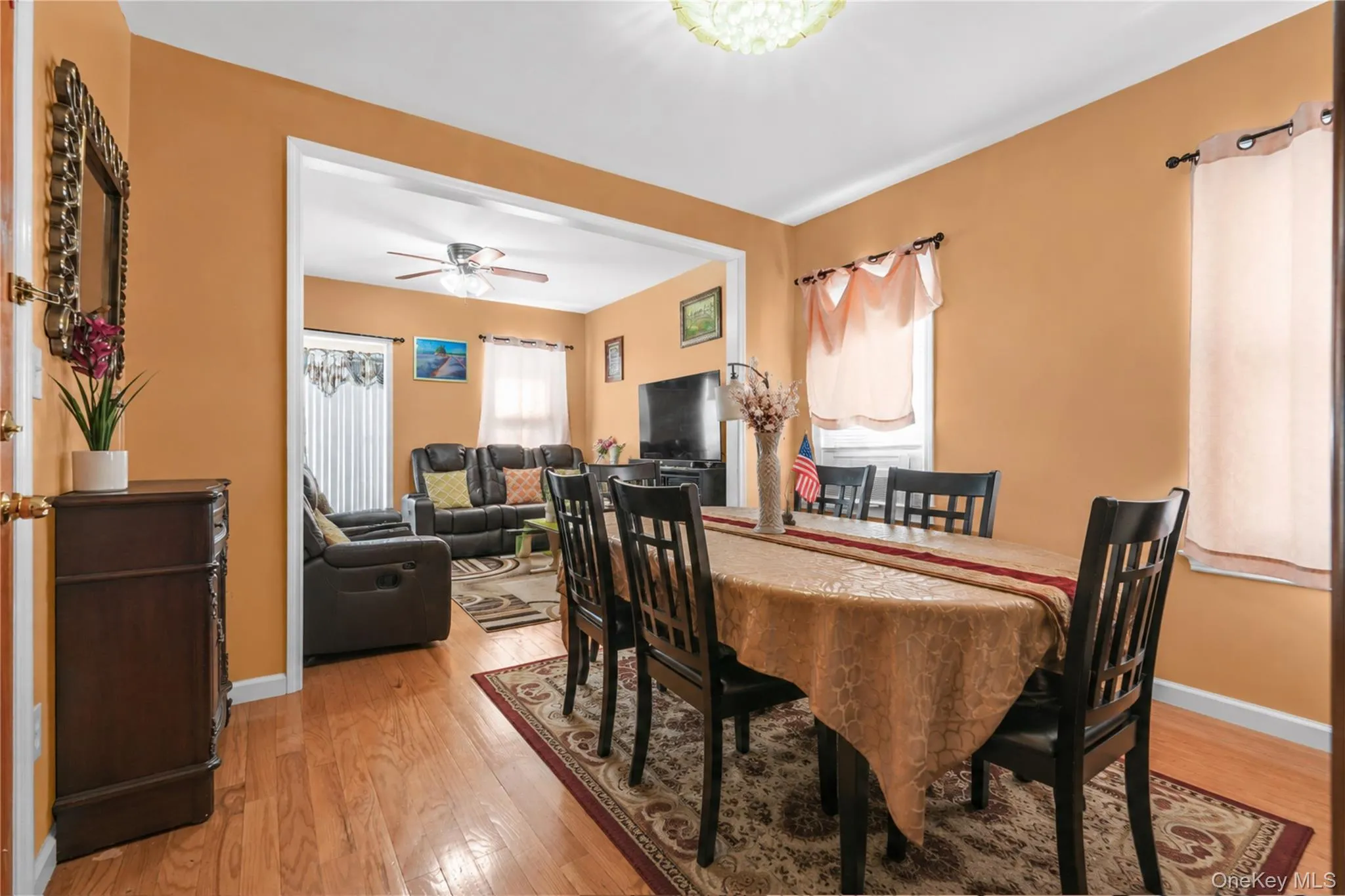 Warm-toned dining space featuring wood-finish flooring, a decorative chandelier, and an open entryway to a living area Warm-toned dining space featuring wood-finish flooring, a decorative chandelier, and an open entryway to a living area