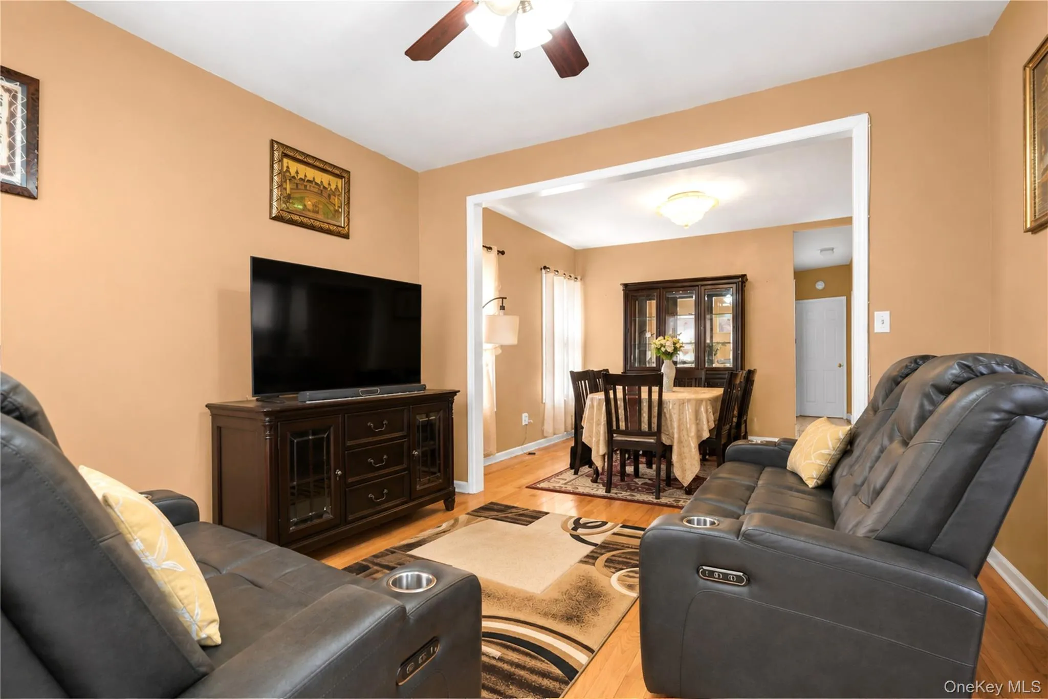 Open-concept living area featuring wood-finish flooring, a ceiling fan with integrated lighting, and a wide entryway into the dining space Open-concept living area featuring wood-finish flooring, a ceiling fan with integrated lighting, and a wide entryway into the dining space