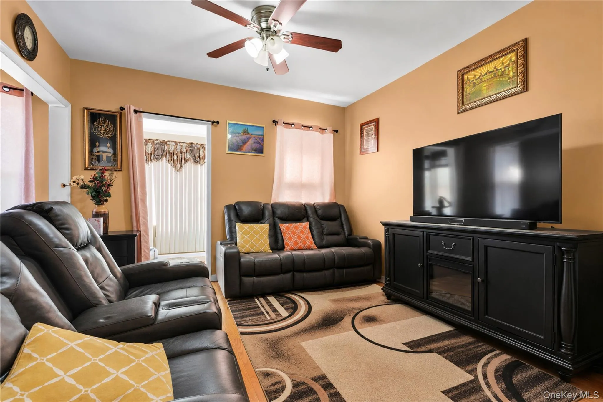Spacious living area featuring warm-toned walls, wood-finish flooring, and a ceiling fan with integrated lighting Spacious living area featuring warm-toned walls, wood-finish flooring, and a ceiling fan with integrated lighting