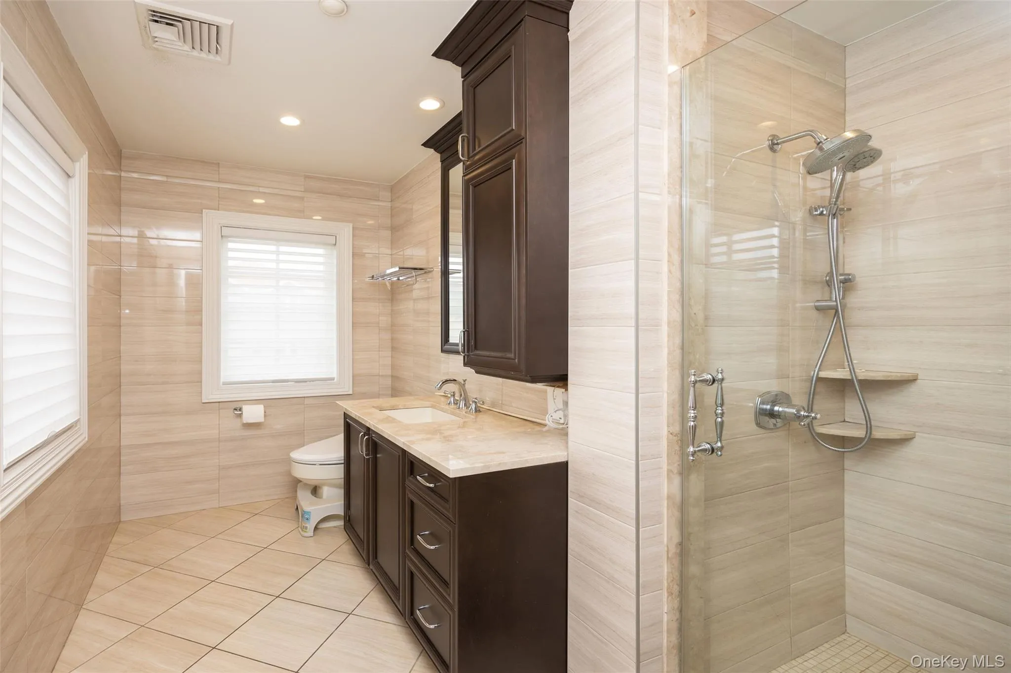 Bathroom featuring tile patterned flooring, a stall shower, toilet, vanity, and tile walls Bathroom featuring tile patterned flooring, a stall shower, toilet, vanity, and tile walls