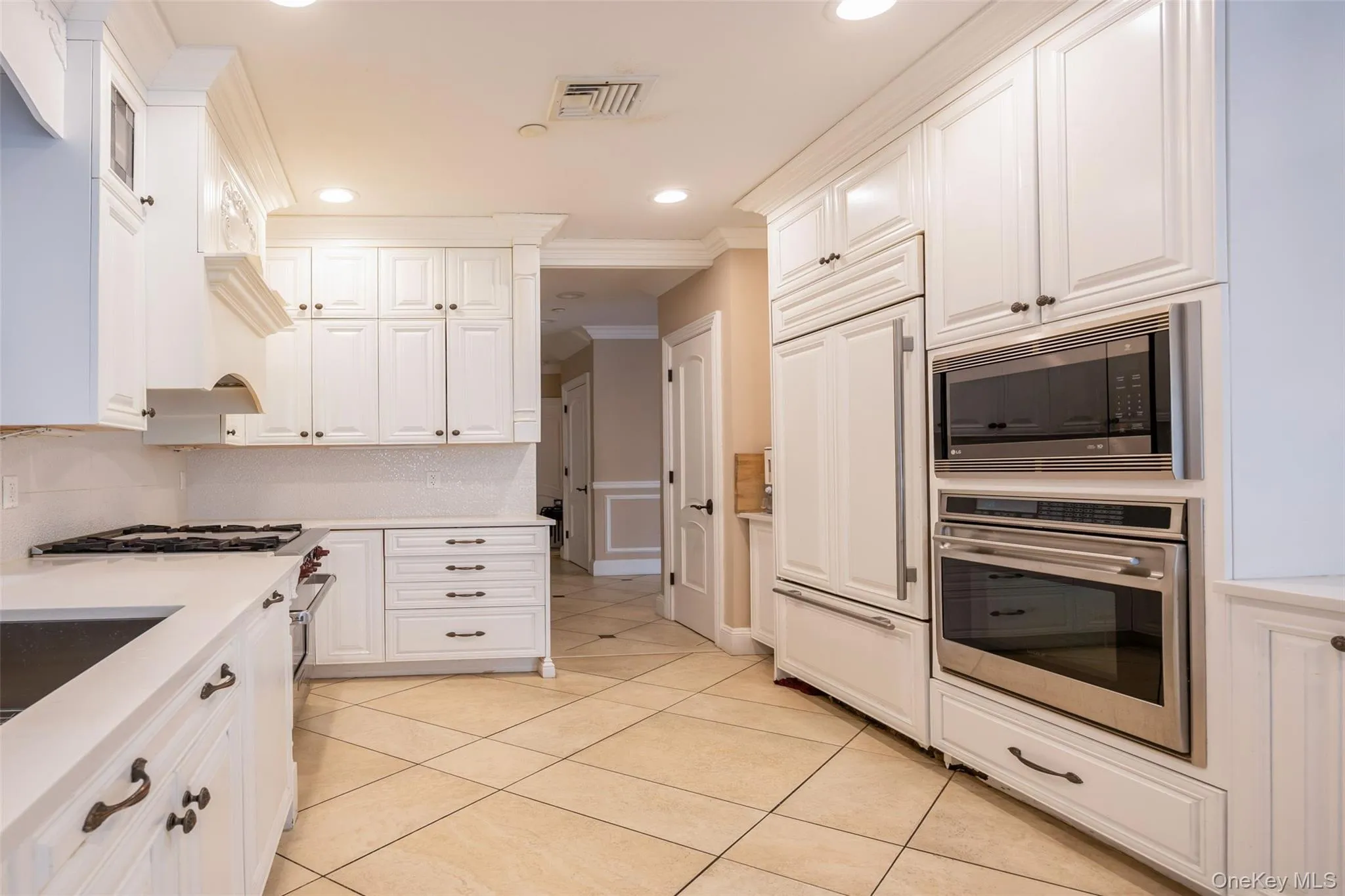 Kitchen featuring built in appliances, crown molding, white cabinets, light tile patterned flooring, and light countertops Kitchen featuring built in appliances, crown molding, white cabinets, light tile patterned flooring, and light countertops