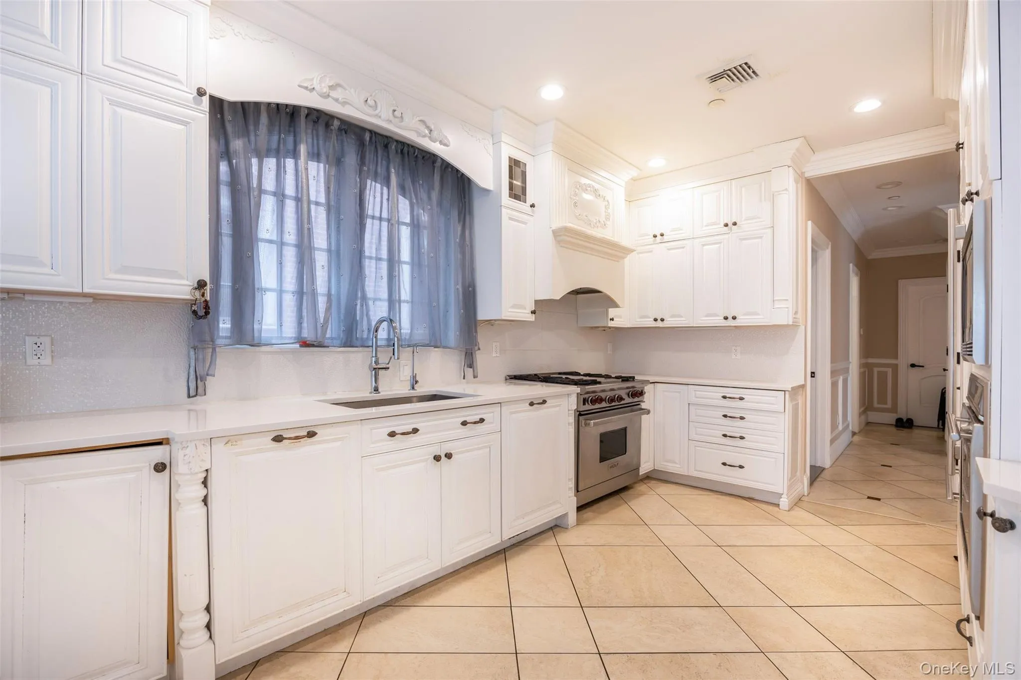 Kitchen featuring high end stainless steel range oven, a sink, crown molding, white cabinetry, and light tile patterned flooring Kitchen featuring high end stainless steel range oven, a sink, crown molding, white cabinetry, and light tile patterned flooring