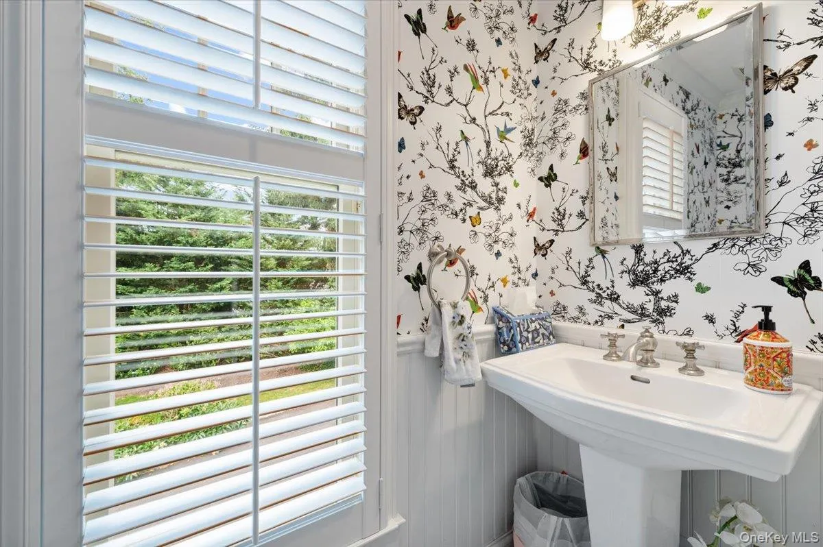Pedestal sink with polished chrome fixtures, framed wall mirror, and decorative wallpaper Pedestal sink with polished chrome fixtures, framed wall mirror, and decorative wallpaper