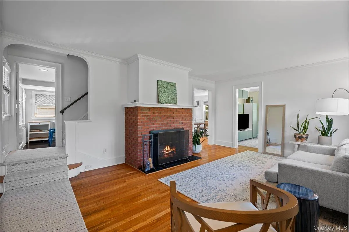 Living room featuring a brick fireplace, hardwood flooring, and bright white walls with crown molding Living room featuring a brick fireplace, hardwood flooring, and bright white walls with crown molding