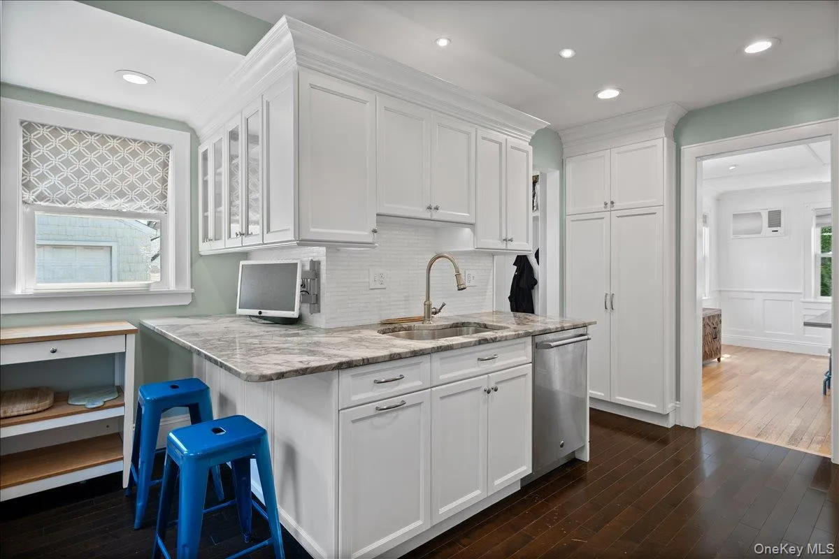 Gourmet kitchen featuring white cabinetry, integrated stainless steel appliances, a tile backsplash, recessed lighting, and rich wood-finish flooring Gourmet kitchen featuring white cabinetry, integrated stainless steel appliances, a tile backsplash, recessed lighting, and rich wood-finish flooring