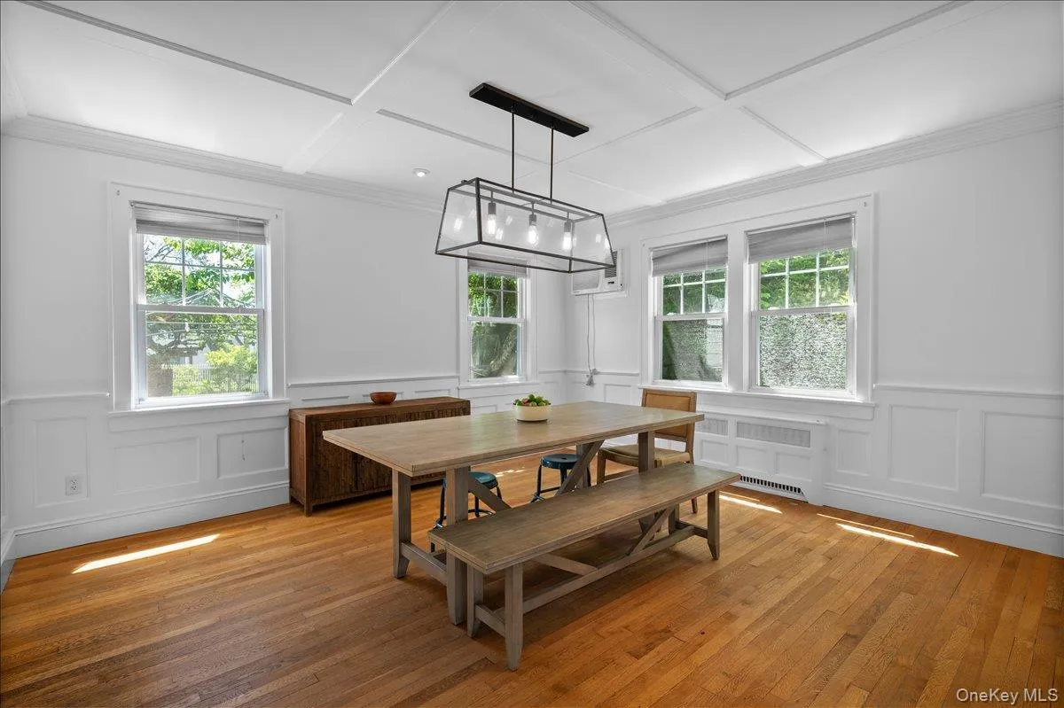 Formal dining space featuring hardwood flooring, white wainscoting, coffered ceiling, and a contemporary linear chandelier Formal dining space featuring hardwood flooring, white wainscoting, coffered ceiling, and a contemporary linear chandelier