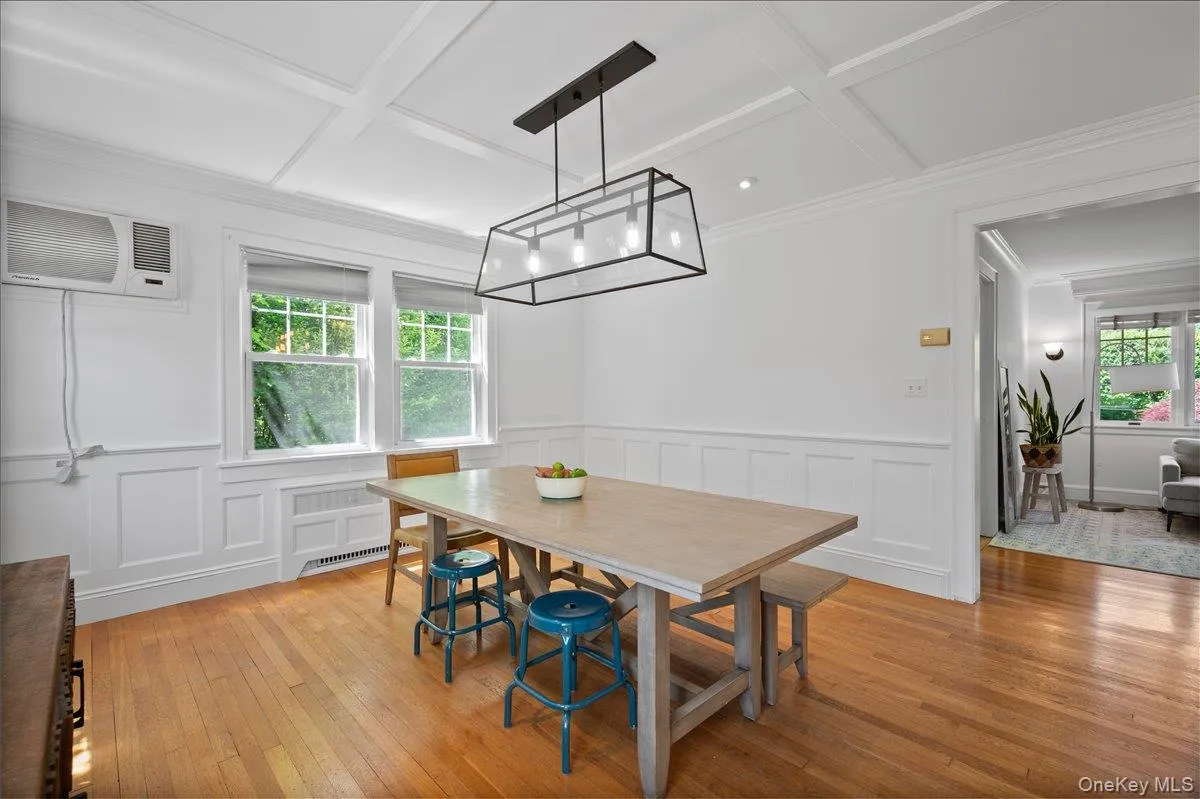Dining space featuring hardwood flooring, coffered ceiling, wainscoting, and a linear pendant light fixture Dining space featuring hardwood flooring, coffered ceiling, wainscoting, and a linear pendant light fixture