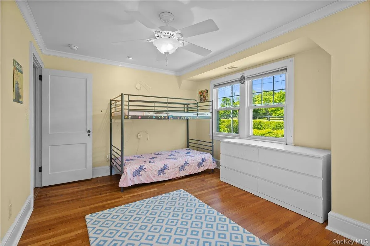 Bedroom #2 with wood-finish flooring, two large windows, a ceiling fan with integrated lighting, and crown molding Bedroom #2 with wood-finish flooring, two large windows, a ceiling fan with integrated lighting, and crown molding
