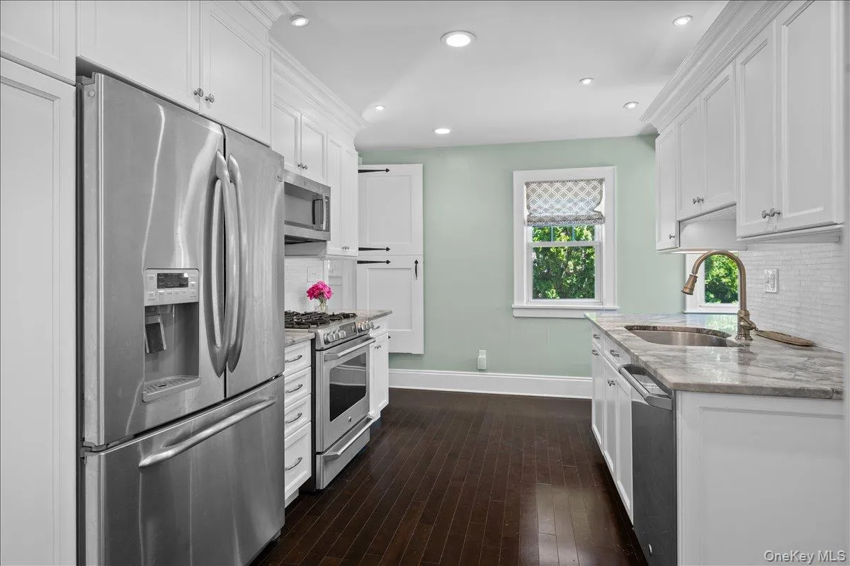 Contemporary kitchen featuring stainless steel appliances, white shaker cabinetry, recessed lighting, wood-finish flooring, and light-toned countertops Contemporary kitchen featuring stainless steel appliances, white shaker cabinetry, recessed lighting, wood-finish flooring, and light-toned countertops
