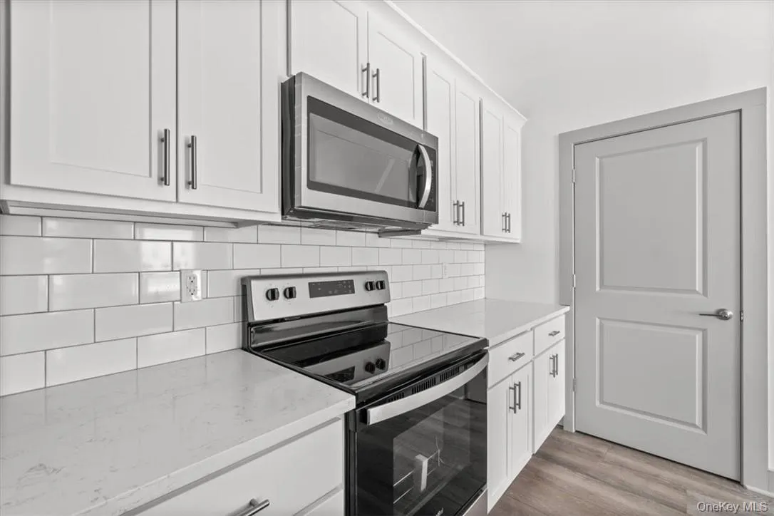 Kitchen with appliances with stainless steel finishes, light hardwood / wood-style floors, decorative backsplash, light stone countertops, and white cabinetry Kitchen with appliances with stainless steel finishes, light hardwood / wood-style floors, decorative backsplash, light stone countertops, and white cabinetry