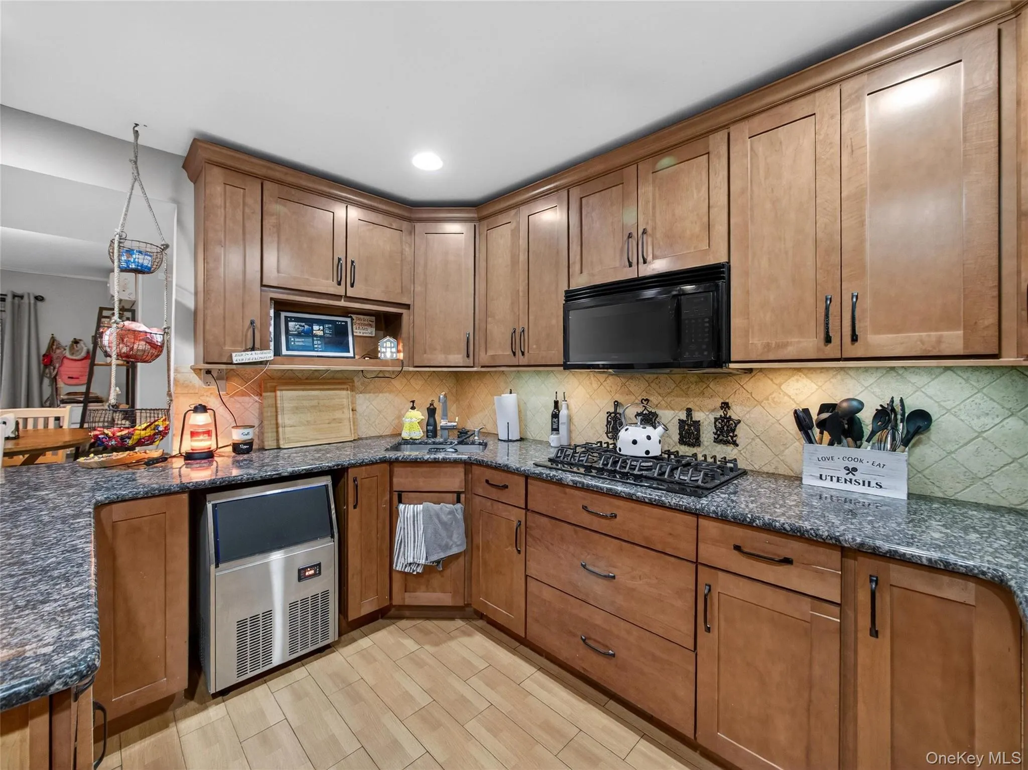 Kitchen featuring brown cabinetry, dark stone countertops, decorative backsplash, and black appliances Kitchen featuring brown cabinetry, dark stone countertops, decorative backsplash, and black appliances