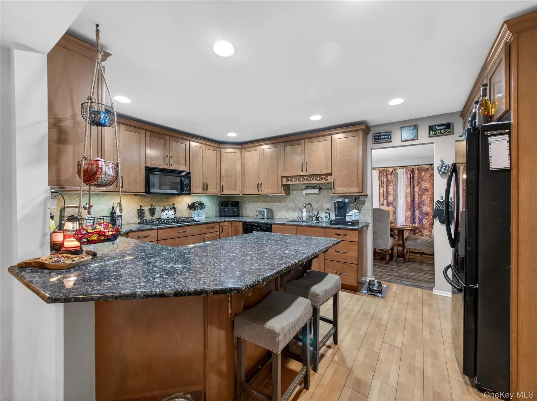 Kitchen featuring a peninsula, dark stone countertops, a breakfast bar area, black appliances, and brown cabinetry Kitchen featuring a peninsula, dark stone countertops, a breakfast bar area, black appliances, and brown cabinetry