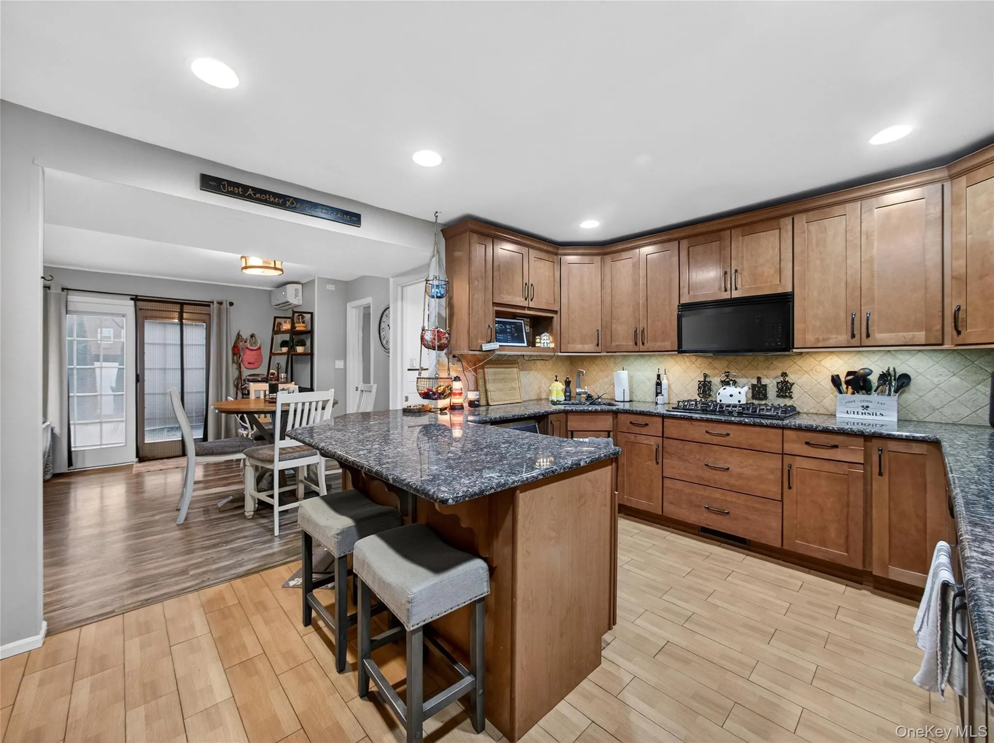Kitchen featuring dark stone counters, a kitchen breakfast bar, brown cabinetry, light wood-style flooring, and recessed lighting Kitchen featuring dark stone counters, a kitchen breakfast bar, brown cabinetry, light wood-style flooring, and recessed lighting