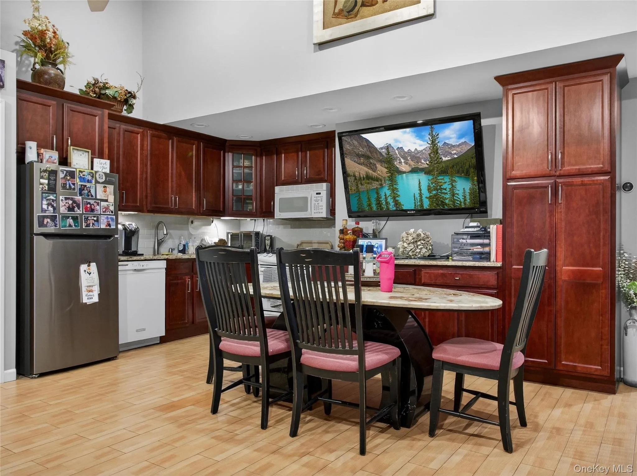 Kitchen featuring white appliances, glass insert cabinets, dark brown cabinets, light stone countertops, and a high ceiling Kitchen featuring white appliances, glass insert cabinets, dark brown cabinets, light stone countertops, and a high ceiling