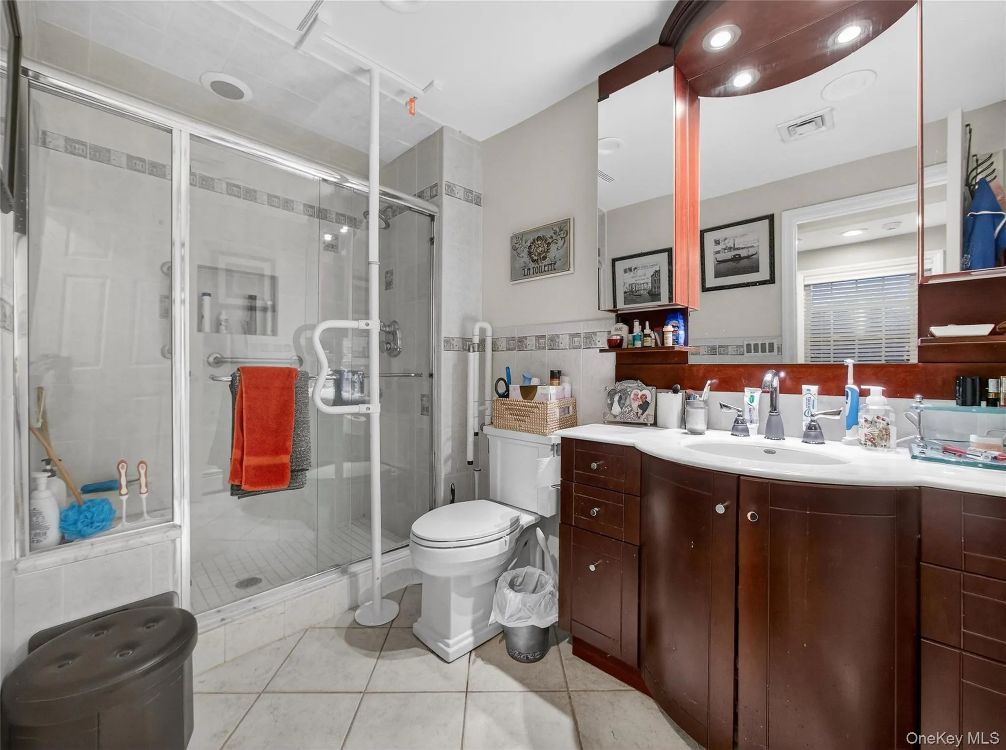 Bathroom featuring vanity, a shower stall, tile walls, light tile patterned floors, and a wainscoted wall Bathroom featuring vanity, a shower stall, tile walls, light tile patterned floors, and a wainscoted wall