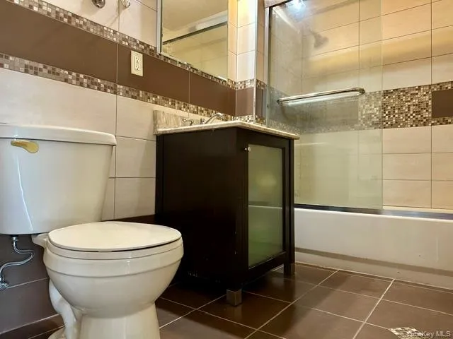 Full bath with vanity, tile wall, shower/tub combo and dark tile patterned floors Full bath with vanity, tile wall, shower/tub combo and dark tile patterned floors