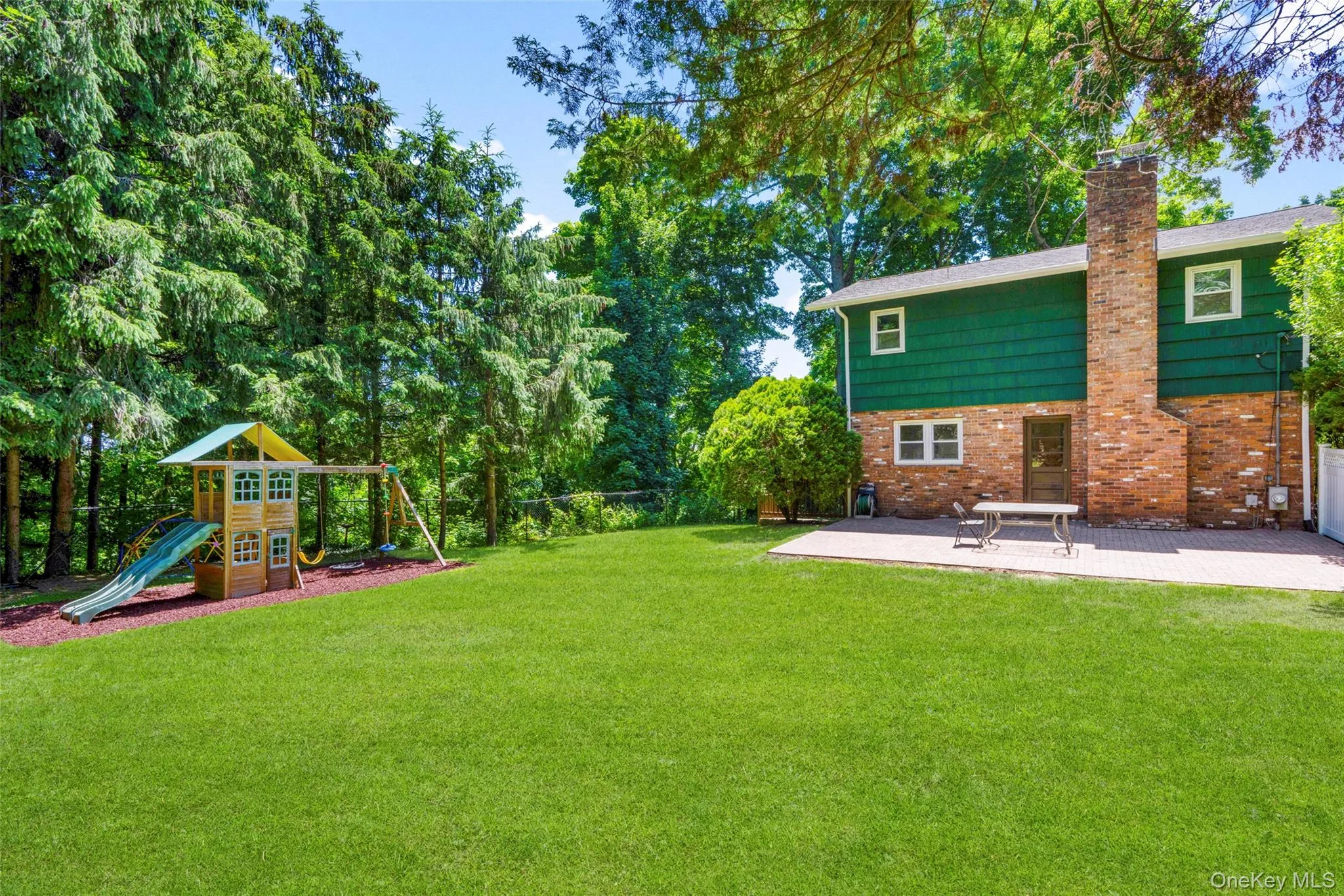 Spacious backyard featuring a large green lawn, a paver patio, brick exterior, and mature perimeter trees Spacious backyard featuring a large green lawn, a paver patio, brick exterior, and mature perimeter trees