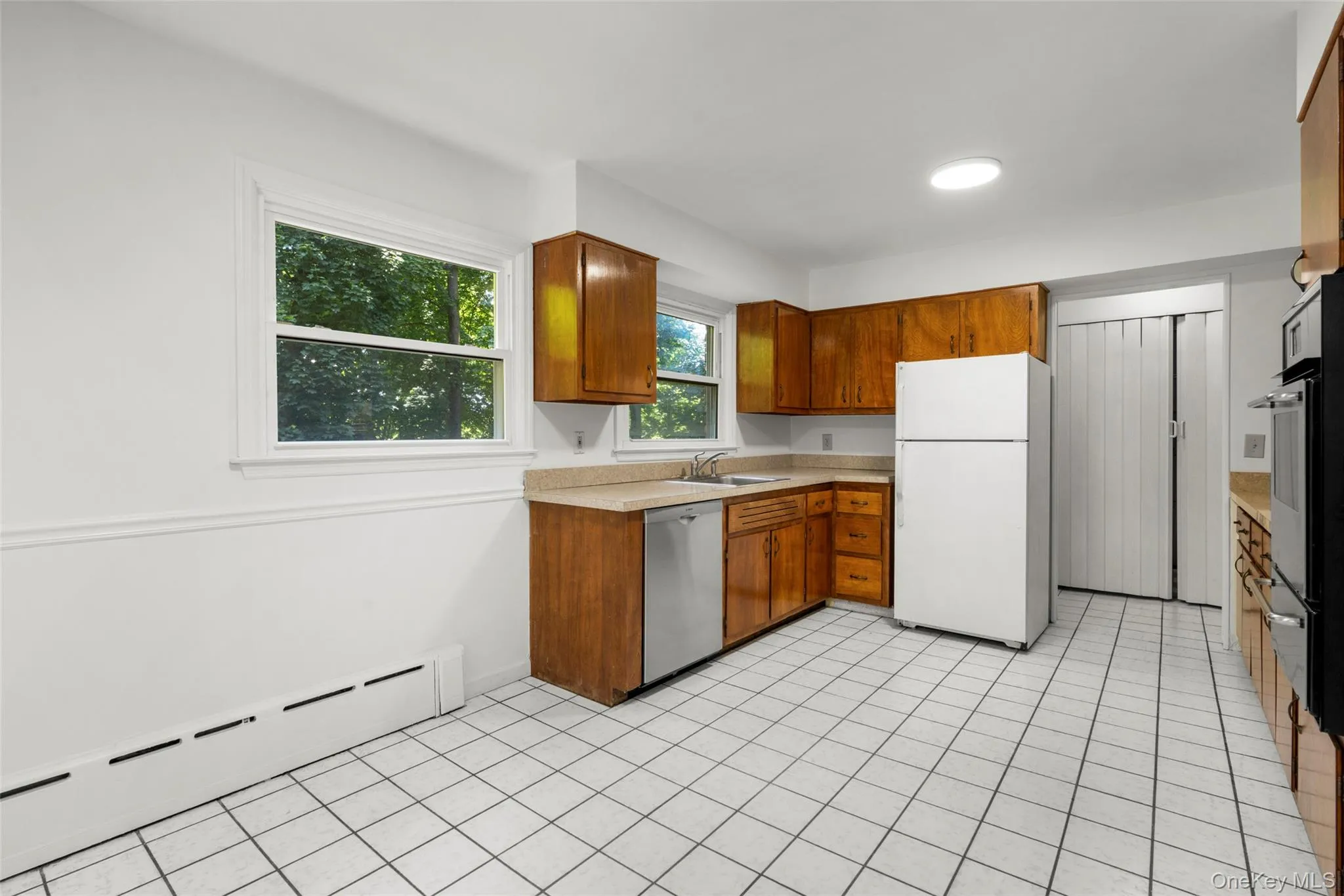 Kitchen featuring wood cabinetry, light-toned countertops, and white square tile flooring Kitchen featuring wood cabinetry, light-toned countertops, and white square tile flooring