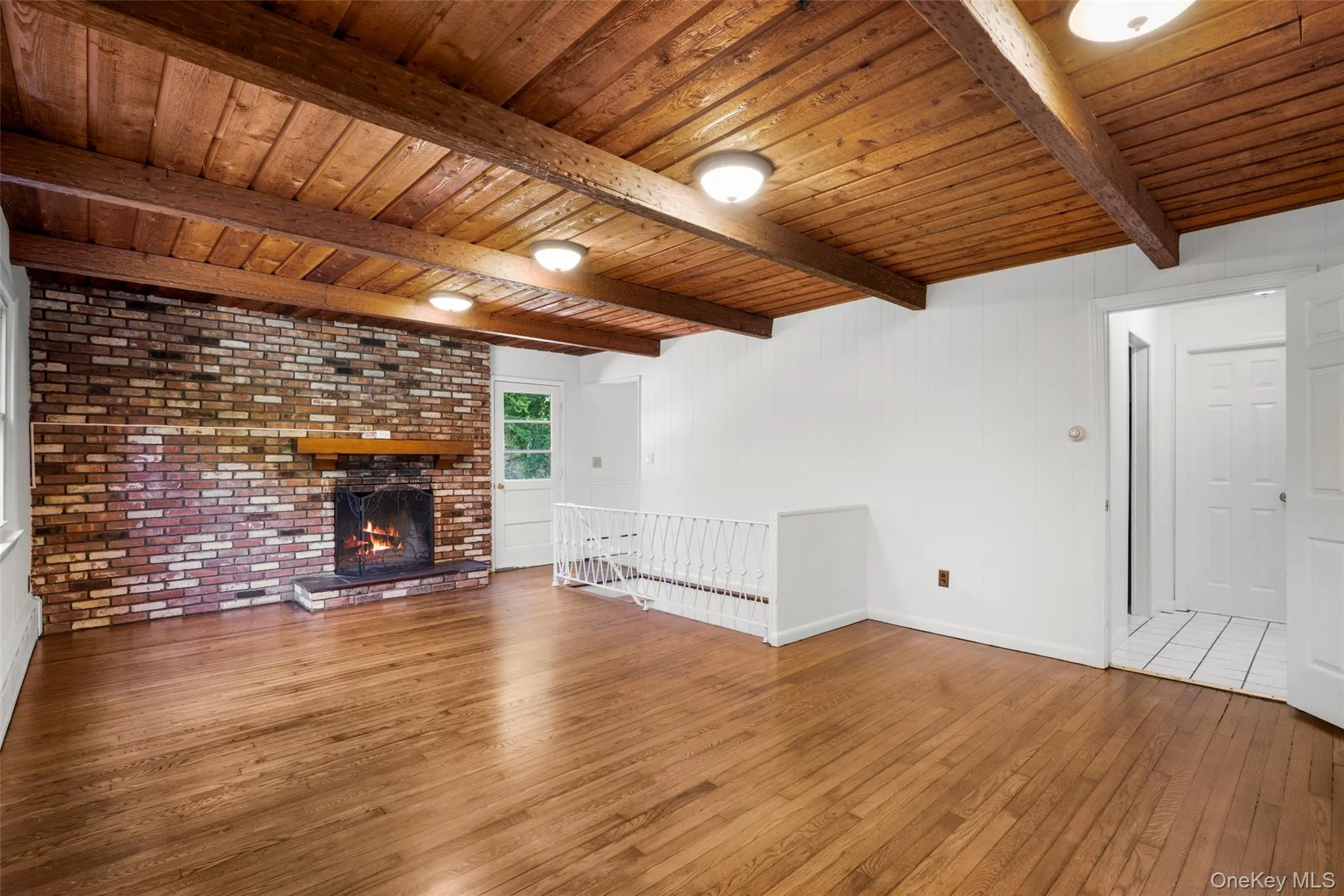 Living area featuring a brick fireplace with a wood mantel, wood-finish flooring, and a wood plank ceiling with exposed beams Living area featuring a brick fireplace with a wood mantel, wood-finish flooring, and a wood plank ceiling with exposed beams