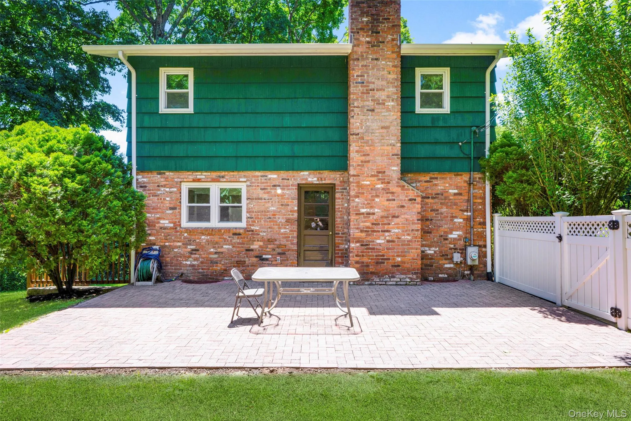 Spacious rear patio constructed with light-toned pavers, complemented by a brick and green siding exterior Spacious rear patio constructed with light-toned pavers, complemented by a brick and green siding exterior