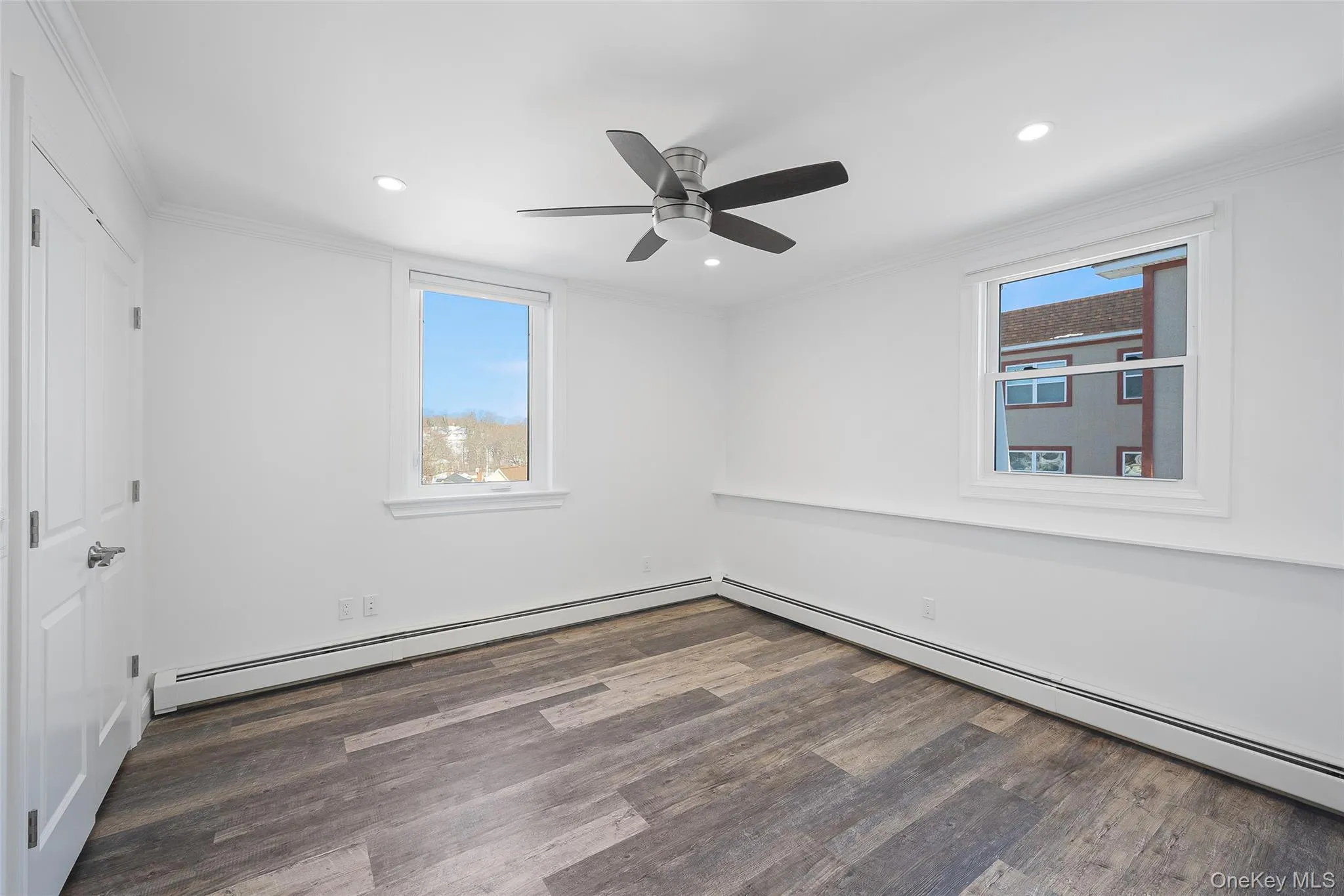 Empty room featuring ceiling fan, a baseboard heating unit, dark wood-type flooring, and crown molding Empty room featuring ceiling fan, a baseboard heating unit, dark wood-type flooring, and crown molding
