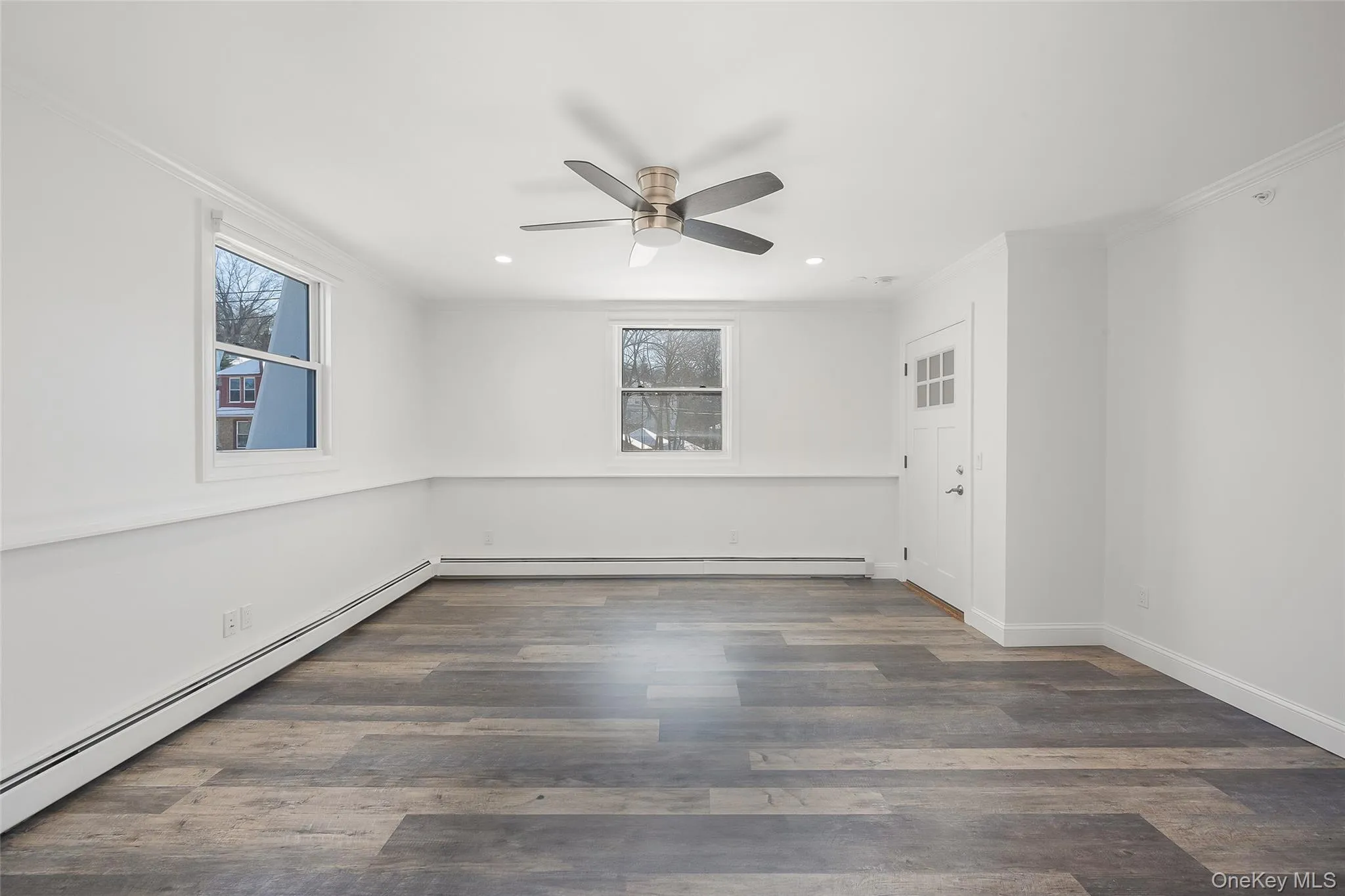 Empty room featuring crown molding, baseboard heating, dark wood-type flooring, and ceiling fan Empty room featuring crown molding, baseboard heating, dark wood-type flooring, and ceiling fan