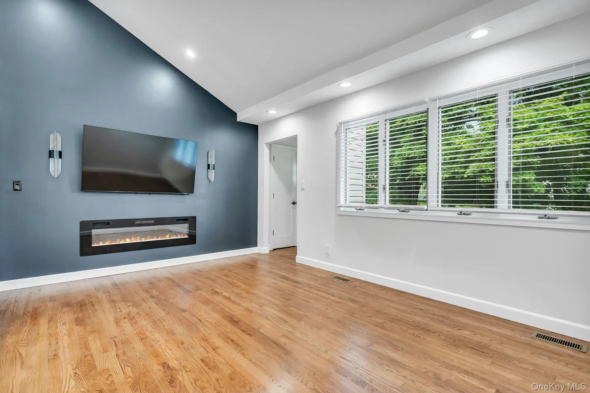 Vaulted ceiling room featuring wood-finish flooring and a built-in electric fireplace Vaulted ceiling room featuring wood-finish flooring and a built-in electric fireplace