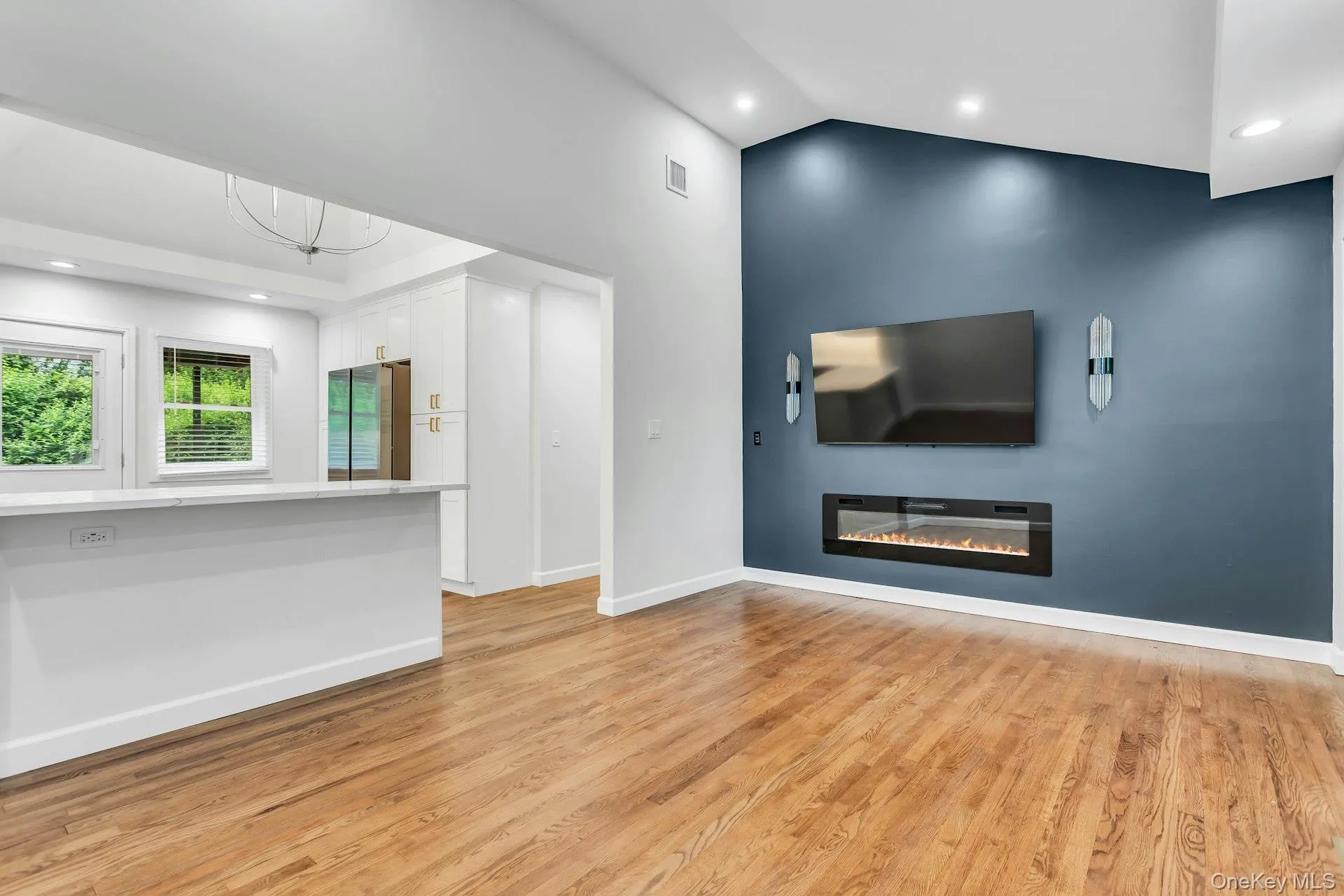 Hardwood flooring throughout featuring a dramatic accent wall with an electric fireplace and wall-mounted sconces Hardwood flooring throughout featuring a dramatic accent wall with an electric fireplace and wall-mounted sconces