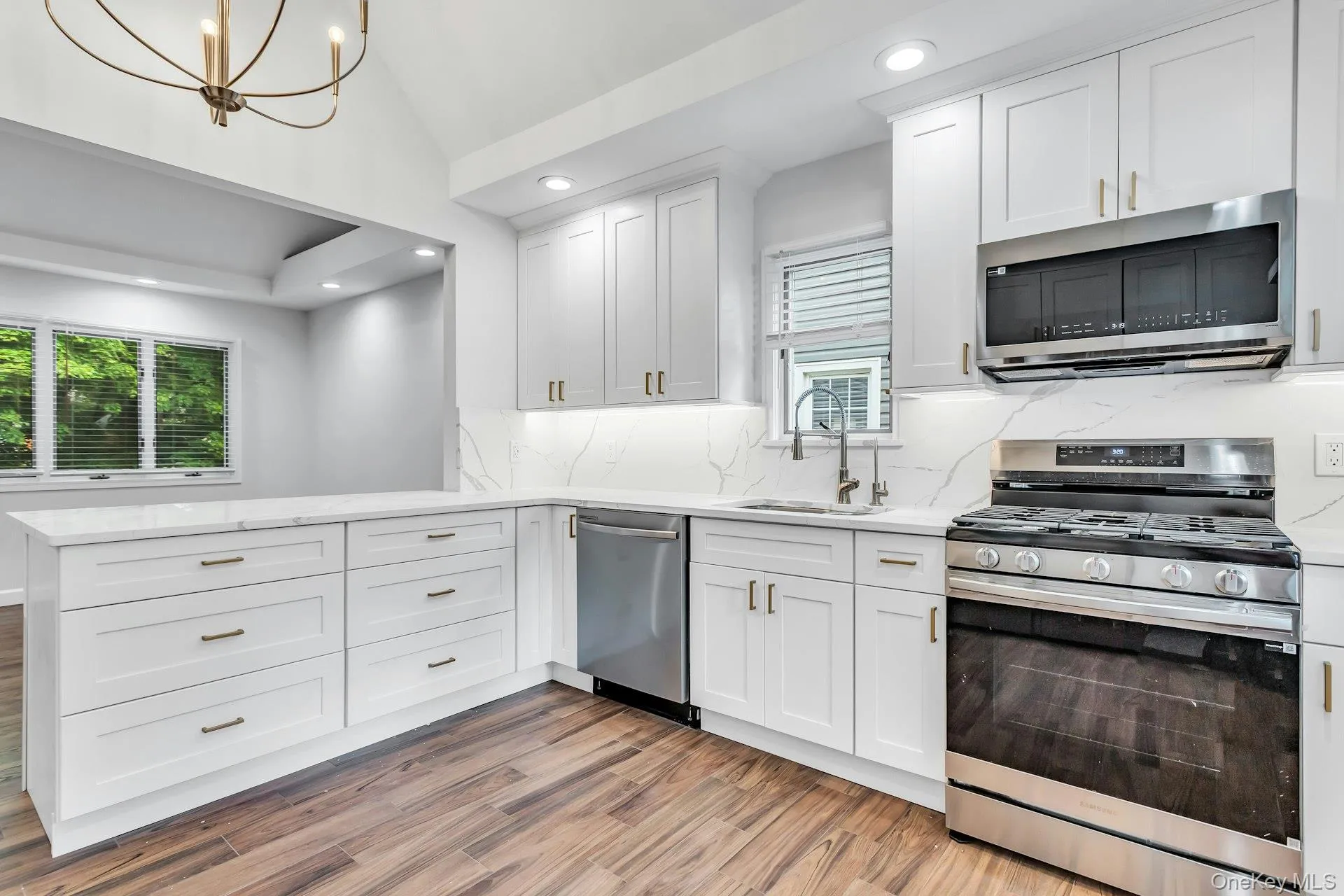 Modern kitchen featuring white shaker cabinetry, gold finished hardware, stainless steel appliances, and wood-finish flooring Modern kitchen featuring white shaker cabinetry, gold finished hardware, stainless steel appliances, and wood-finish flooring