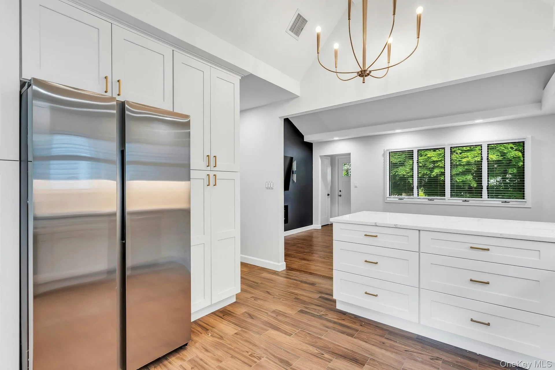 Kitchen featuring white cabinetry with gold-toned hardware, a large stainless steel refrigerator, and wood-finish flooring Kitchen featuring white cabinetry with gold-toned hardware, a large stainless steel refrigerator, and wood-finish flooring