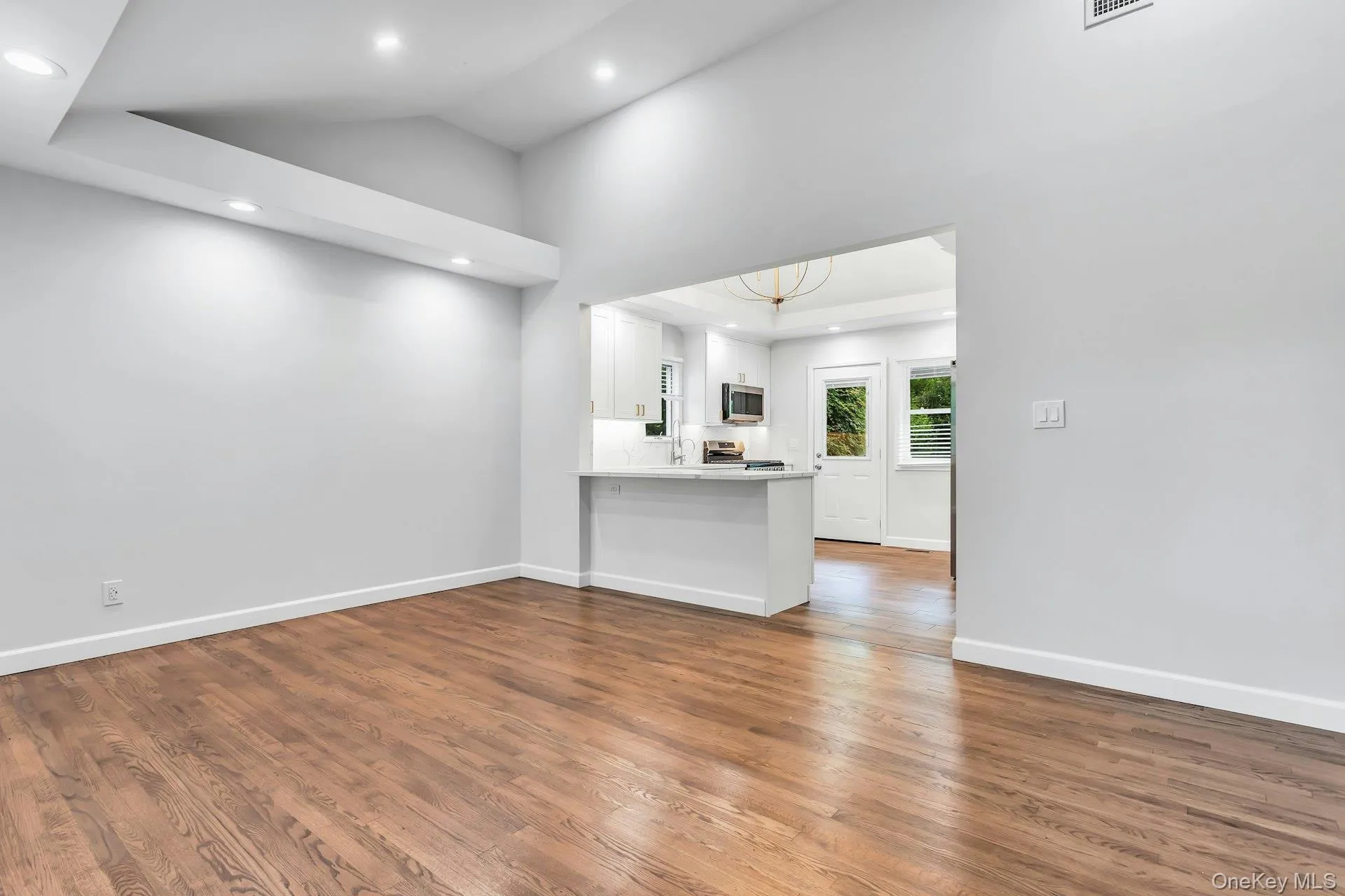 Spacious room featuring wood-finish flooring, recessed lighting, and vaulted ceilings Spacious room featuring wood-finish flooring, recessed lighting, and vaulted ceilings