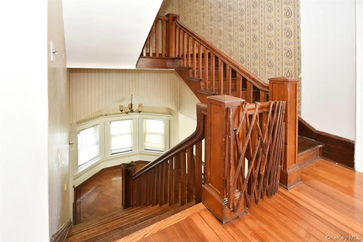 Staircase with a chandelier, wood finished floors, and wallpapered walls Staircase with a chandelier, wood finished floors, and wallpapered walls