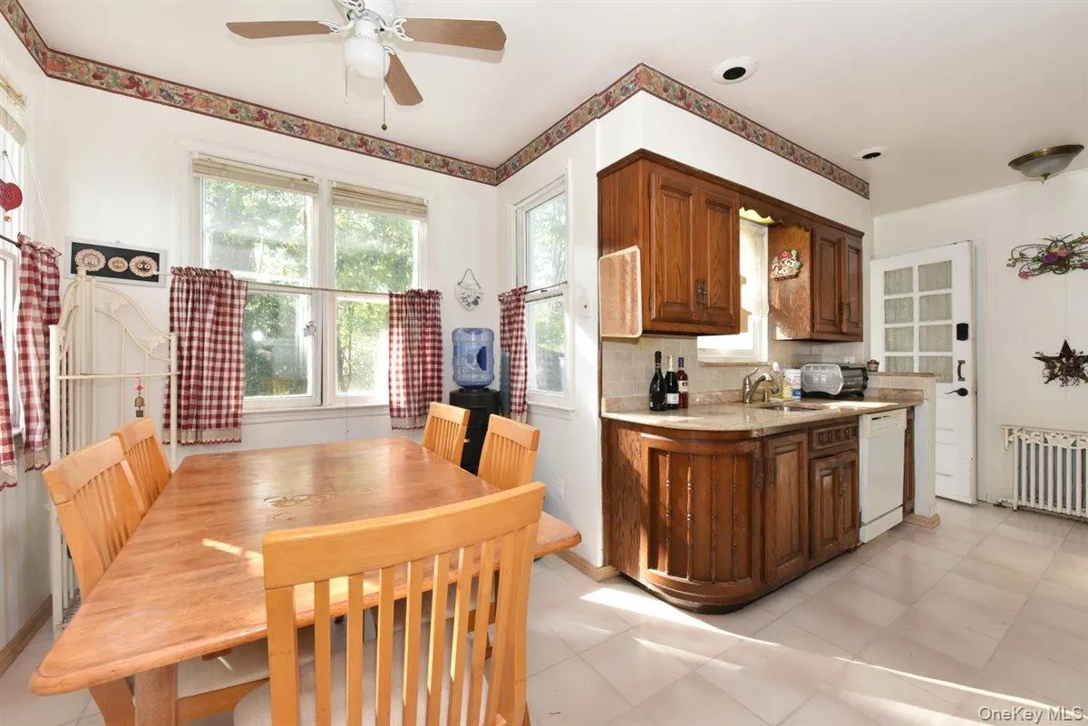 Kitchen featuring decorative backsplash, radiator heating unit, white dishwasher, a ceiling fan, and light stone countertops Kitchen featuring decorative backsplash, radiator heating unit, white dishwasher, a ceiling fan, and light stone countertops