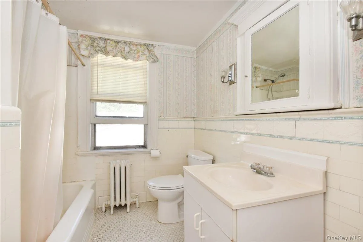 Full bathroom with wallpapered walls, radiator heating unit, tile walls, vanity, and light tile patterned floors Full bathroom with wallpapered walls, radiator heating unit, tile walls, vanity, and light tile patterned floors