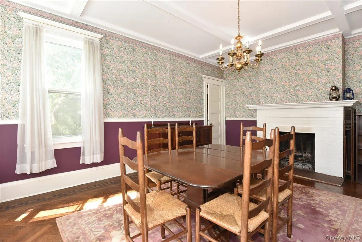 Dining area featuring beamed ceiling, wallpapered walls, a fireplace with raised hearth, and a chandelier Dining area featuring beamed ceiling, wallpapered walls, a fireplace with raised hearth, and a chandelier