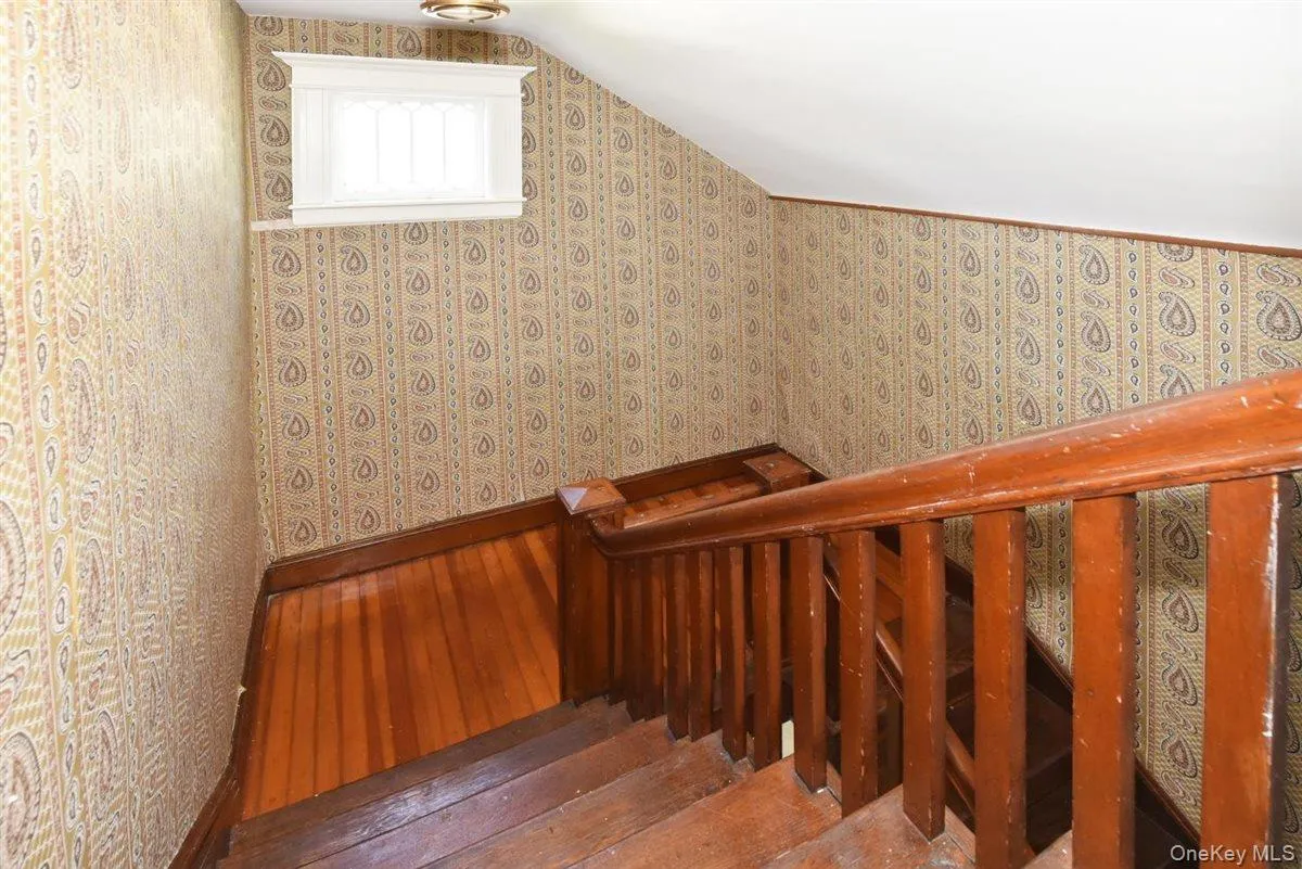 Stairs with wood-type flooring, vaulted ceiling, and wallpapered walls Stairs with wood-type flooring, vaulted ceiling, and wallpapered walls