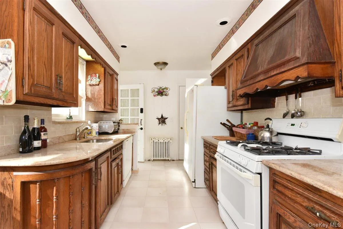 Kitchen featuring tasteful backsplash, white appliances, custom exhaust hood, and radiator heating unit Kitchen featuring tasteful backsplash, white appliances, custom exhaust hood, and radiator heating unit